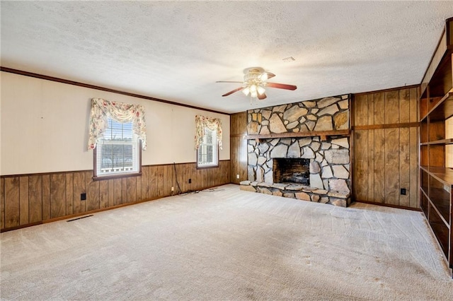 unfurnished living room with ceiling fan, a textured ceiling, light carpet, a stone fireplace, and wood walls