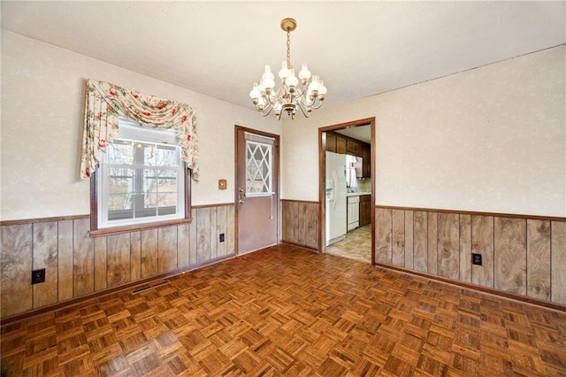 empty room with an inviting chandelier, dark parquet flooring, and wood walls