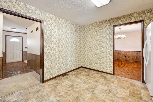 spare room with parquet floors, a chandelier, a textured ceiling, and wood walls