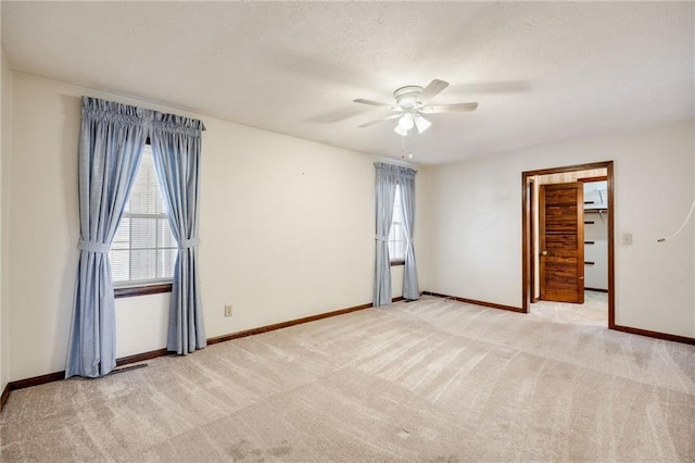 spare room with a textured ceiling, light colored carpet, and ceiling fan