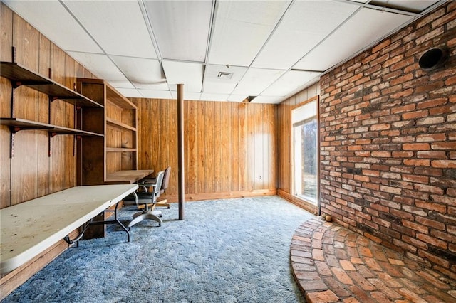 unfurnished office featuring a paneled ceiling, light colored carpet, and wood walls