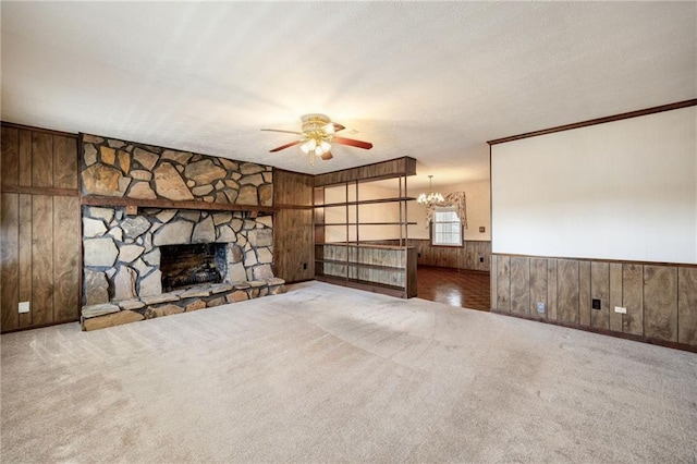 unfurnished living room with wooden walls, carpet flooring, ceiling fan with notable chandelier, and a stone fireplace