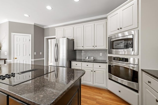 kitchen featuring crown molding, appliances with stainless steel finishes, dark stone countertops, white cabinets, and light wood-type flooring