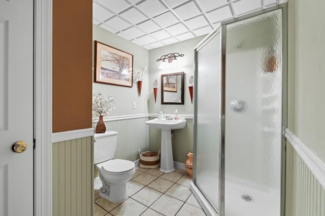 bathroom with tile patterned flooring, an enclosed shower, toilet, and a drop ceiling