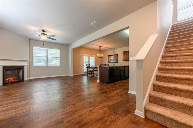 unfurnished living room featuring ceiling fan with notable chandelier and dark hardwood / wood-style flooring