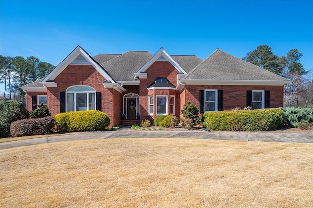 view of front of home with roof with shingles, a front yard, and brick siding