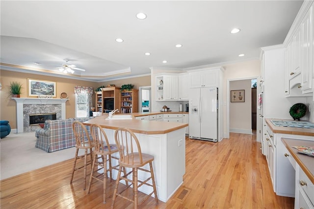 kitchen with a breakfast bar area, a high end fireplace, open floor plan, a sink, and white fridge with ice dispenser