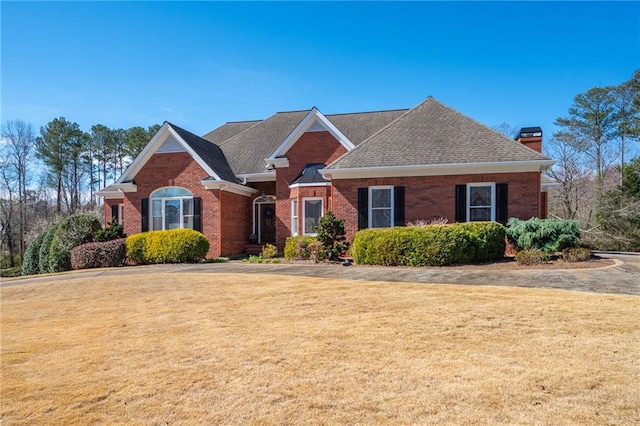 view of front facade with a front yard, brick siding, a chimney, and roof with shingles