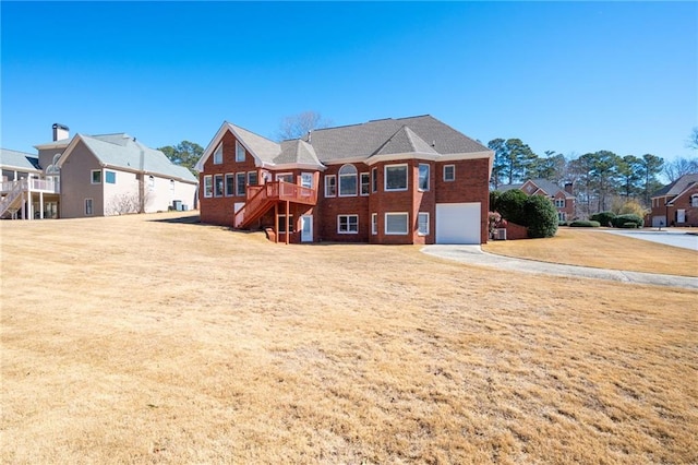 back of property featuring a lawn, a residential view, an attached garage, stairs, and brick siding