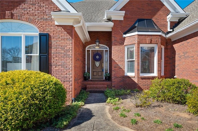 property entrance with a shingled roof and brick siding