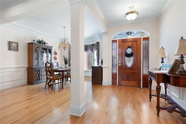 entryway featuring ornate columns, light wood-style flooring, ornamental molding, and a chandelier