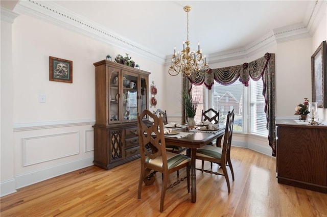 dining area with a chandelier, a wainscoted wall, ornamental molding, and light wood finished floors