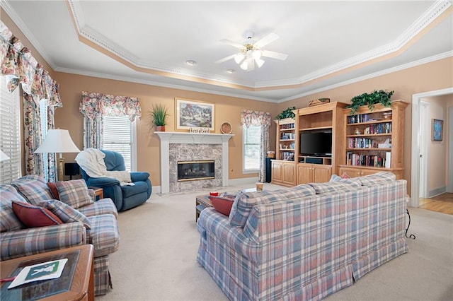 living area with light carpet, a fireplace, baseboards, ornamental molding, and a tray ceiling