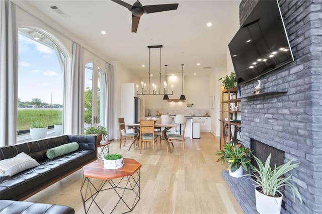 living room featuring ceiling fan with notable chandelier, a fireplace, and light hardwood / wood-style flooring