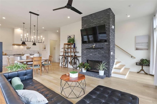 living room featuring a fireplace, ceiling fan with notable chandelier, and light hardwood / wood-style flooring