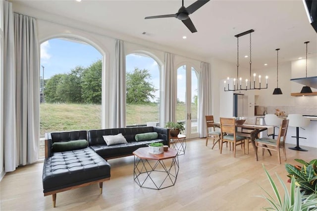 living room featuring ceiling fan with notable chandelier, a healthy amount of sunlight, and light wood-type flooring