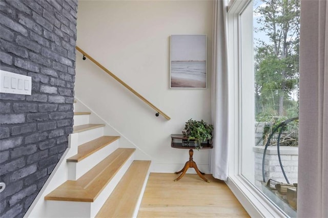 staircase featuring brick wall, plenty of natural light, and wood-type flooring