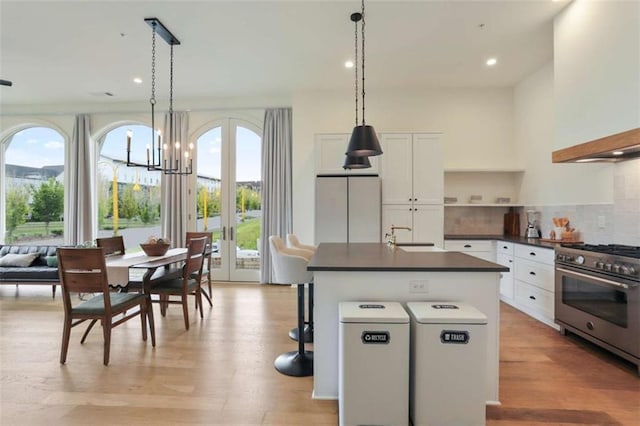 kitchen with tasteful backsplash, a center island with sink, white cabinets, and high end range