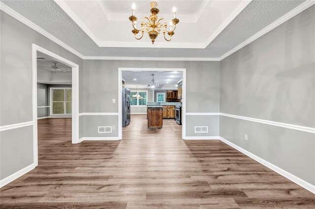 unfurnished dining area featuring hardwood / wood-style flooring, a chandelier, and a raised ceiling