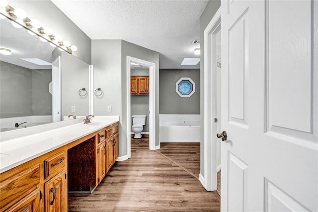 bathroom with vanity, wood-type flooring, a skylight, toilet, and a textured ceiling