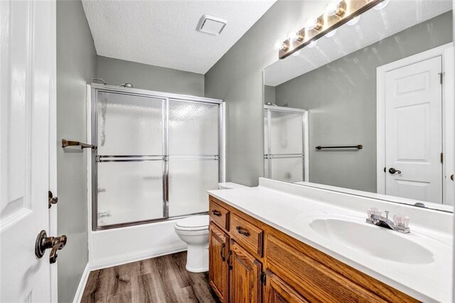 full bathroom featuring vanity, wood-type flooring, a textured ceiling, bath / shower combo with glass door, and toilet