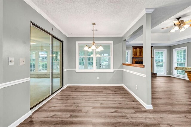 unfurnished dining area with ceiling fan with notable chandelier, crown molding, wood-type flooring, and a textured ceiling