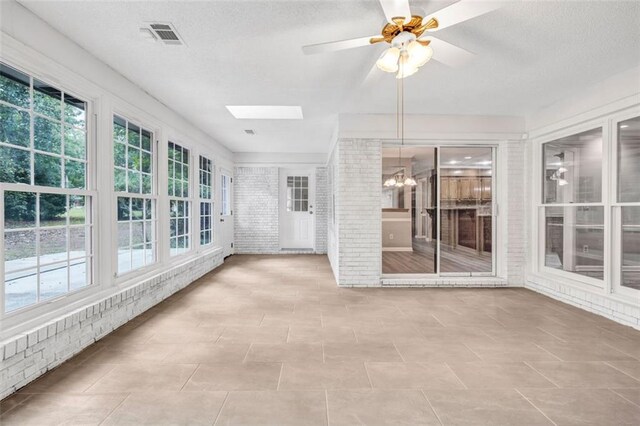 unfurnished sunroom featuring ceiling fan with notable chandelier and a skylight