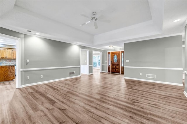 unfurnished living room with ceiling fan, light hardwood / wood-style flooring, and a raised ceiling