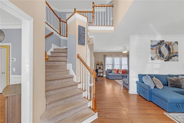 staircase featuring a ceiling fan, ornamental molding, and wood finished floors