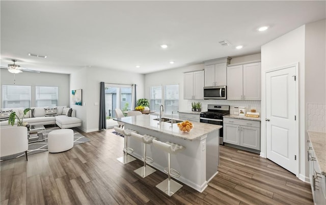 kitchen with light stone countertops, sink, stainless steel appliances, an island with sink, and a kitchen bar