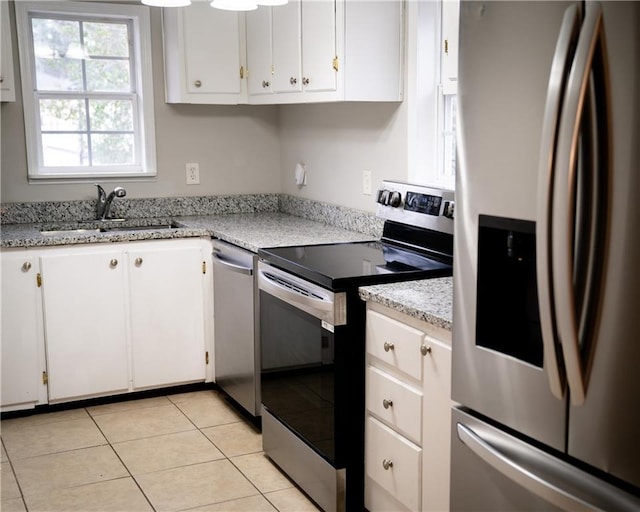 kitchen featuring appliances with stainless steel finishes, light stone counters, sink, light tile patterned floors, and white cabinetry