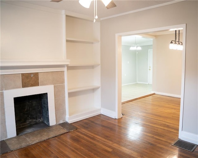 unfurnished living room featuring ceiling fan with notable chandelier, wood-type flooring, built in features, and a fireplace