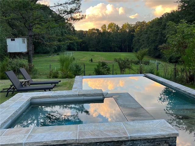 pool at dusk featuring a yard, a patio area, and a storage unit