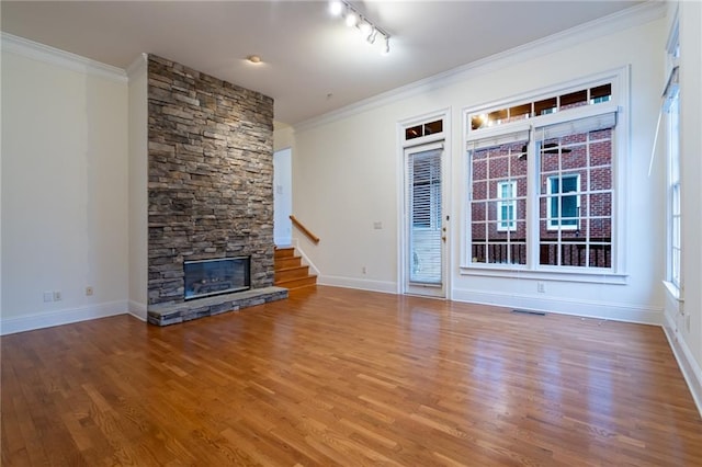 unfurnished living room with hardwood / wood-style flooring, crown molding, a stone fireplace, and track lighting