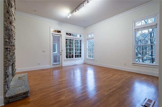 unfurnished room featuring ornamental molding, plenty of natural light, dark wood-type flooring, and a stone fireplace