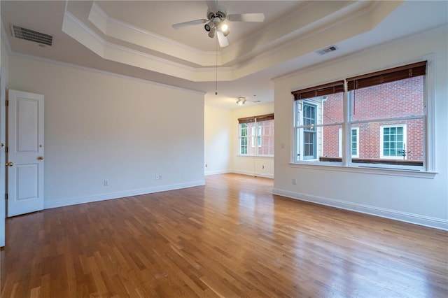 empty room featuring hardwood / wood-style flooring, ornamental molding, a raised ceiling, and ceiling fan