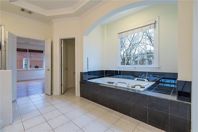 bathroom featuring tile patterned flooring, ornamental molding, tiled bath, and a tray ceiling