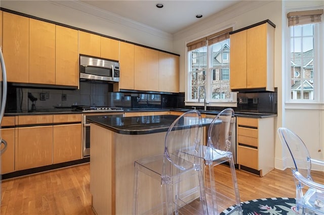 kitchen featuring appliances with stainless steel finishes, backsplash, ornamental molding, a kitchen island, and light wood-type flooring