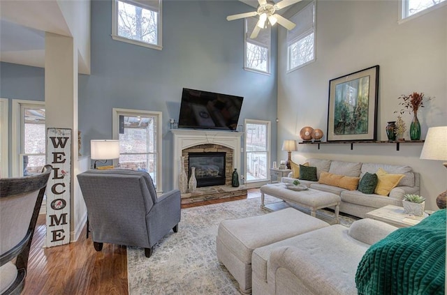 living room featuring a fireplace, wood-type flooring, ceiling fan, and a high ceiling