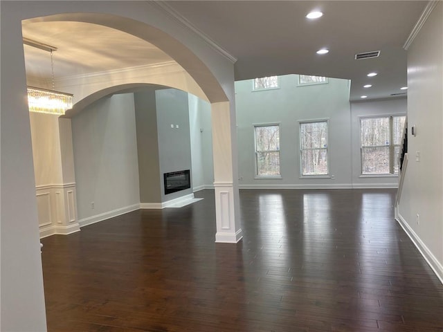 unfurnished living room featuring dark wood-style floors, recessed lighting, visible vents, ornamental molding, and a glass covered fireplace