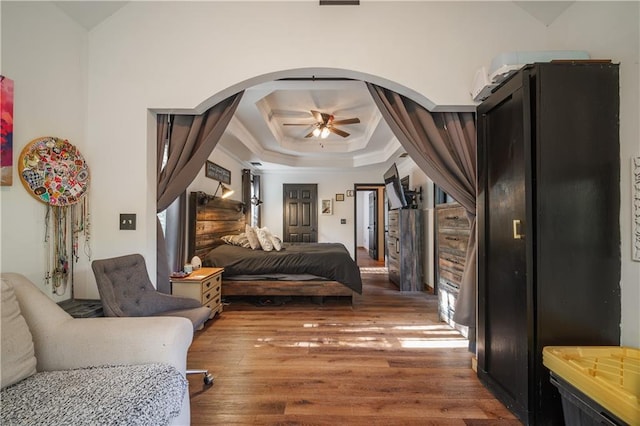 bedroom with hardwood / wood-style flooring, a raised ceiling, and ceiling fan