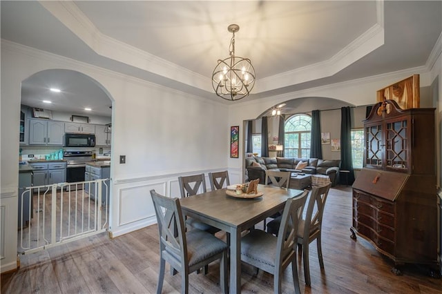 dining space with a raised ceiling, a notable chandelier, crown molding, and light hardwood / wood-style floors