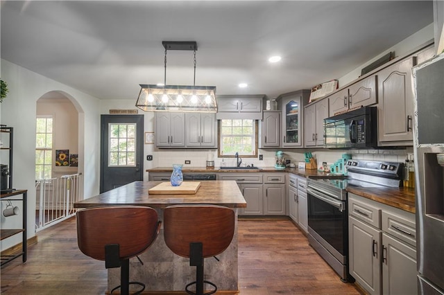 kitchen with gray cabinets, stainless steel appliances, butcher block countertops, a kitchen island, and sink