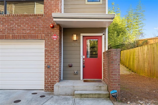 entrance to property with brick siding, a garage, and fence