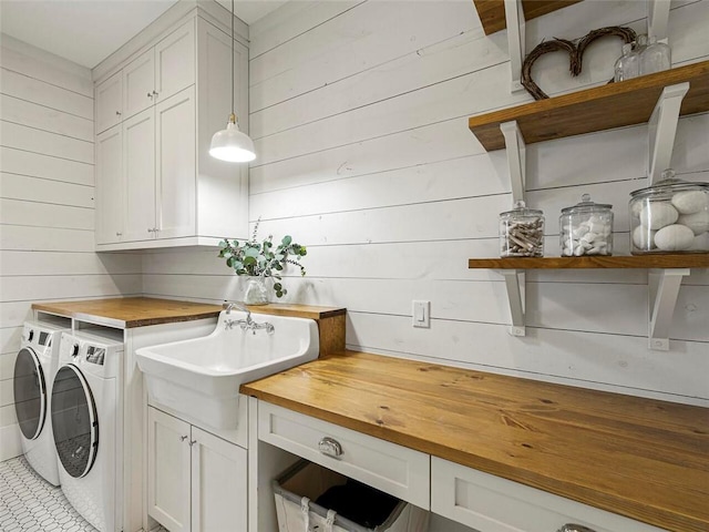 laundry room featuring a sink, wood walls, cabinet space, and washing machine and clothes dryer
