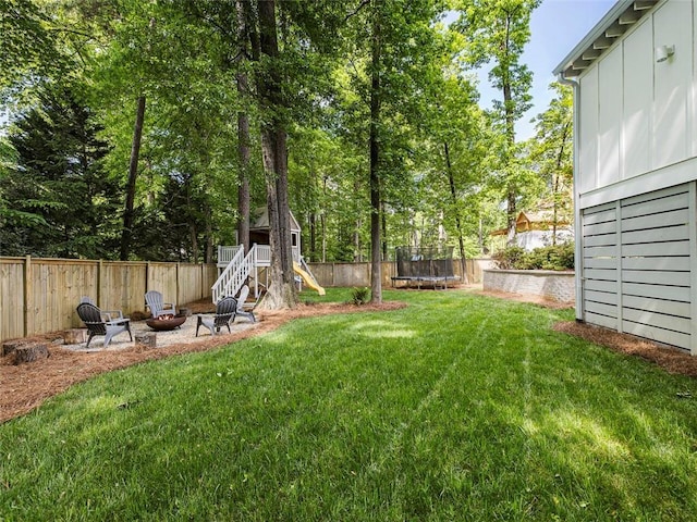 view of yard with a fenced backyard, a trampoline, and a fire pit