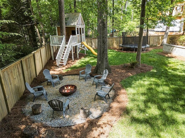view of yard with a playground, a trampoline, a fenced backyard, and an outdoor fire pit