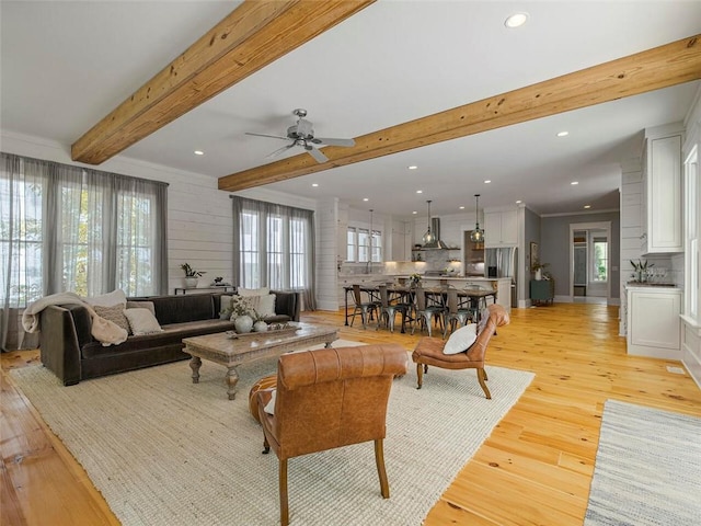 living room featuring a ceiling fan, beamed ceiling, recessed lighting, and light wood-style flooring