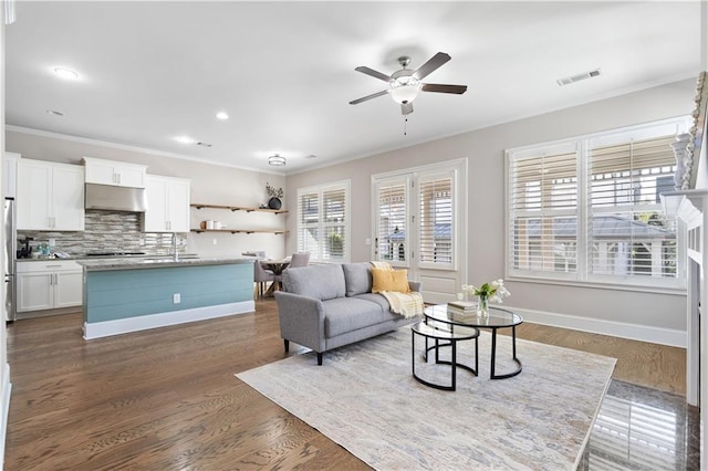 living area with baseboards, visible vents, dark wood finished floors, and crown molding