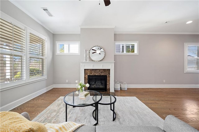 living room with wood finished floors, a high end fireplace, visible vents, baseboards, and crown molding